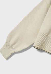 Maglione a maglia color beige chiaro con polsini a costine e una texture liscia. La manica presenta una vestibilità rilassata con dettagli di cucitura sottili.