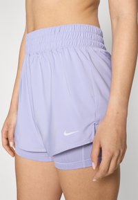 Pantalones cortos deportivos de color morado claro con una cinturilla elástica fruncida. Incluye una capa interna y un pequeño logo blanco de Nike en el dobladillo.