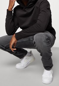 Felpa con cappuccio nera, jeans grigi e scarpe da ginnastica bianche. La felpa ha un design semplice, mentre i jeans presentano una vestibilità slim. Le scarpe hanno una suola testurizzata.