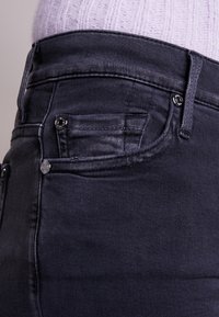 Donkerdenim jeans met een gladde textuur, vijf zakken en zilveren hardwaredetails. De stof toont subtiele stiksels en een nauwsluitend ontwerp.
