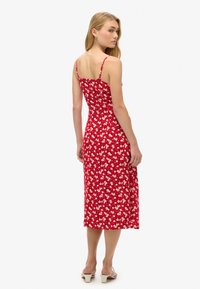 Rotes Blumenkleid mit dünnen Trägern, knielang, tailliertem Oberteil und leicht ausgestelltem Rock. Mit kleinen weißen und rosa Blumenmuster.