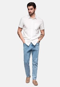 Witte korte mouwen overhemd met een borstzak, gecombineerd met lichtblauwe jeans en beige instapschoenen, wat een klassieke, casual stijl laat zien.
