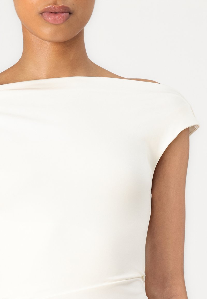 Top blanc dénudé sur les épaules avec une texture lisse et extensible, et des coutures minimales. Présente un design ajusté et un drapé doux au niveau du décolleté.