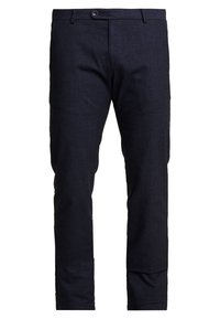 Pantalon bleu marine en matière texturée, avec braguette zippée, fermeture par bouton et coupe ajustée. Lignes épurées et absence de motifs visibles.