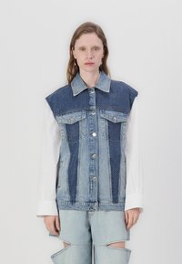 Denim vest featuring a dark blue polka dot yoke, large collar, front pockets, and silver buttons, paired with light blue distressed jeans.