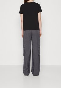 Camiseta de algodón negra con cuello redondo, combinada con pantalones cargo grises de corte amplio con bolsillos laterales y una tela texturizada.