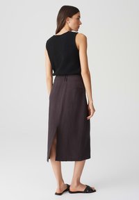 Top noir sans manches avec une finition texturée, associé à une longue jupe gris foncé à fente sur le côté et une poche arrière unique.