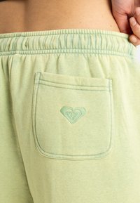 Lys grønne joggingbukser med elastisk talje, der har en enkelt baglomme og en hjerteformet broderet detalje i samme farve.