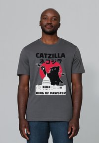 Grijze katoenen t-shirt met een grafisch ontwerp van een reusachtige kat tegen een rode cirkel, met de tekst "CATZILLA" en "KING OF PAWSTER" eronder.