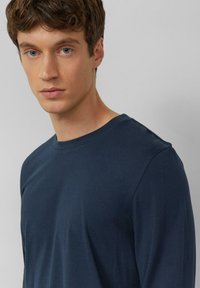 Marineblauw T-shirt met lange mouwen van zachte stof, voorzien van een ronde hals en een getailleerd ontwerp met een gladde textuur en minimale stikseldetails.