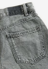 Hallid denim püksid, millel on tagatasku, nähtav õmblus, tekstureeritud kangas ning pleekinud pesu vöökoha ja tasku piirkonnas.