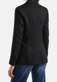 Svart texturerad kavaj med skräddarsydd passform, långärmad, med slagkrage och sidofickor. Bärs tillsammans med blå denimjeans.