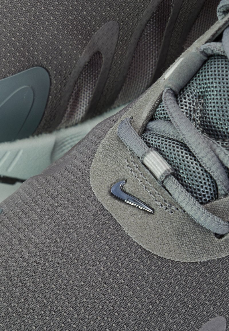 Zapatillas Nike en gris oscuro, con tejido texturizado, acentos de malla y un logo brillante. El diseño incluye curvas pronunciadas y una suela sólida.