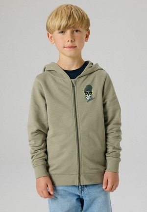 Vaaleanvihreä vetoketjullinen huppari, jossa edessä pääkallokuvio, valmistettu pehmeästä puuvillamateriaalista, ja jossa on resorit hihansuissa sekä kiristysnyörit huppuosassa.