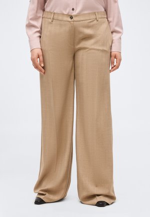 Beežid laia säärega püksid vööaasadekste, ees nööpide ja tõmblukuga, kantud kahvatu roosa pikkade varrukatega särgiga ja mustade kingadega.