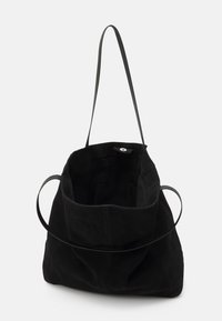 Sac tote en daim noir avec une texture douce, une bandoulière unique et un sommet ouvert. Doté d'un bouton en métal rond à l'intérieur pour la fermeture.