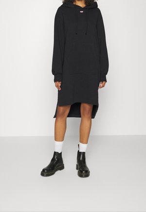 Vestito in felpa nero con cappuccio, maniche lunghe, tasca frontale e spacchi laterali; indossato con stivaletti neri alla caviglia e calze bianche.