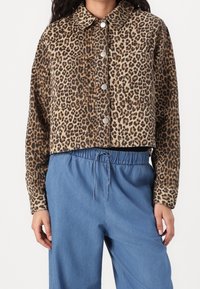 Korte jas met luipaardprint van zacht textiel, voorzien van zilveren knopen en twee voorzakken. Gecombineerd met lichtblauwe broek met elastische taille.