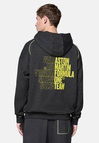 Czarna bluza z kapturem z dużą grafiką w kolorze żółtym na plecach. Posiada zielone przeszycia, kaptur na sznurki oraz luźny krój.