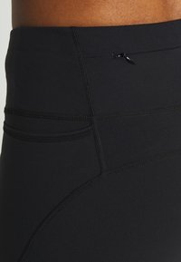 Schwarze Sportleggings mit glatter Textur, hohem Bund und Flachnähten. Enthält eine kleine Tasche mit Reißverschluss.
