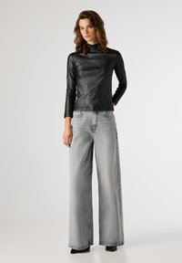 Μαύρο μακρύ μανίκι μπλούζα με υφή και λαμπερό φινίρισμα, συνδυασμένη με ανοιχτό γκρι παντελόνι φαρδιάς γραμμής. Το σύνολο διαθέτει εφαρμοστή σιλουέτα και ελάχιστες λεπτομέρειες.