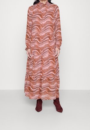 Mujer con un vestido largo de manga larga y cuello alto, con rayas onduladas en tonos rosa y marrón, combinado con botines de tacón en color rojo oscuro.