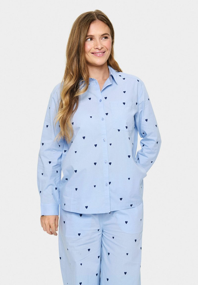 Camicia di cotone blu chiaro con motivo a cuori navy, abbottonatura frontale e colletto. Maniche lunghe con polsini abbottonati e taschino singolo sul petto.