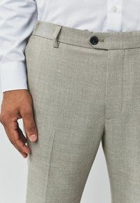 Light gray tailored pants made from textured fabric, featuring a single button closure and flat front design, with visible crease lines.