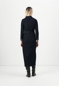 Robe chemise en denim foncé avec des manches longues, une taille ceinturée et une silhouette droite, présentant un col classique et des poignets à boutons.