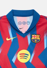 Tricou de fotbal roșu și albastru cu guler în V, imprimat cu logo-ul Nike, emblemă Spotify și un blazon cu dungi orizontale și o minge.