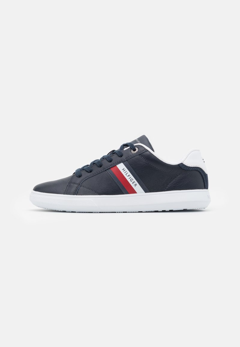 Baskets en cuir bleu marine avec une semelle en caoutchouc blanche, dotées de lacets bleu foncé et d'accents rayés rouge, blanc et gris sur le côté.