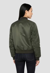 Olijfgroene bomberjack met een gladde, glanzende afwerking, geribde manchetten en tailleband. Voorzien van een ritssluiting en een getailleerde pasvorm.