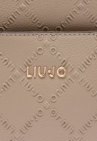 Borsa a tracolla in pelle beige con logo "LIU·JO" impresso. Dettagli in metallo dorato e superficie testurizzata con motivi geometrici.