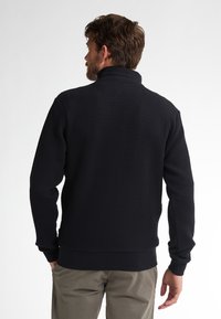 Pullover blu navy con un motivo tessuto texturizzato, colletto alto e polsini e orlo a costine. Vestibilità sagomata visibile dalla vista posteriore.
