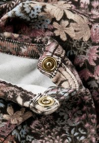 Materiał w kwiatowy wzór w odcieniach różu, niebieskiego i beżu; posiada złote metalowe zatrzaski oraz miękkie, teksturowane krawędzie.