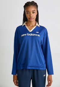 Kék hosszú ujjú sportpóló bézs gallérral, hálós textúrával és fehér "new balance" logóval az elején.