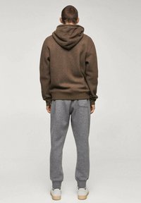 Sweat à capuche marron à finition texturée, associé à un pantalon de survêtement gris. Les deux vêtements présentent une coupe décontractée et des poignets élastiques.