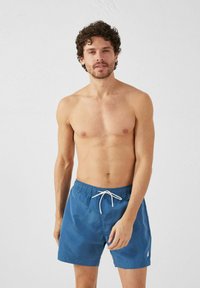 Pantaloni da bagno blu realizzati in materiale leggero, con vita elastica e cordoncino bianco, arricchiti da un piccolo logo.