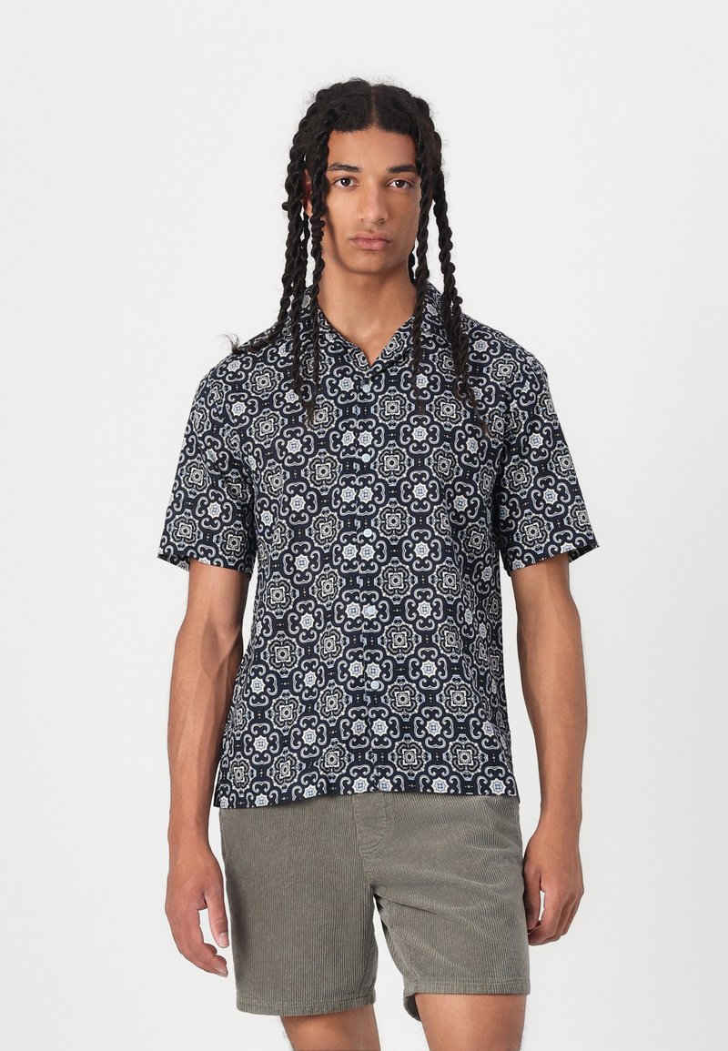 Chemise à manches courtes en bleu marine avec un motif, dotée d'un col. Associée à un short en velours côtelé vert olive.