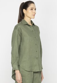 Szalony zielony, zapięty na guziki koszula z lekkiego, teksturowanego materiału z kołnierzykiem w kształcie ostrego, jedną kieszenią na piersi i zaokrąglonym dołem.