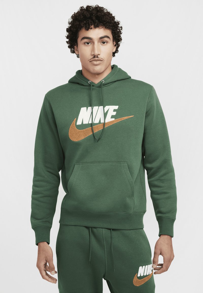 Felpa verde realizzata in tessuto morbido, con un logo Nike bianco e un logo Swoosh dorato. Include una tasca a canguro frontale e un cordino regolabile.