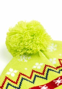 Cappello lavorato a maglia di un brillante verde, caratterizzato da un grande pompon, motivi a zigzag in rosso e blu, e motivi di fiocchi di neve bianchi. Materiale morbido e testurizzato.