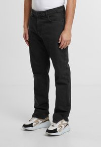 Blugi negri din denim cu croială dreaptă, cinci buzunare și o textură netedă. Purtați cu adidași distinctivi multicolori.