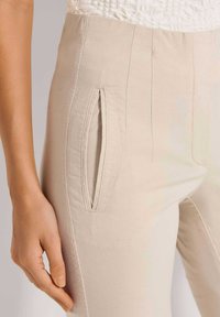 Beige broek van een gestructureerde stof, met zijzakken en getailleerde naden voor een passende look. Close-up van de detaillering van de zak.