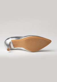 Zapato de tacón alto plateado con punta afilada, suela de goma texturizada y parte superior brillante. El tacón presenta un diseño pequeño y redondeado antideslizante.