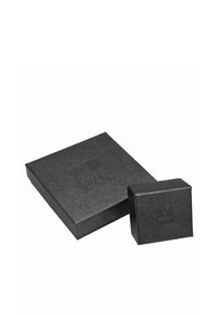 Dos cajas de cartón negras, una más grande y rectangular con un logo, y una caja más pequeña cuadrada, ambas con textura mate y diseño minimalista.