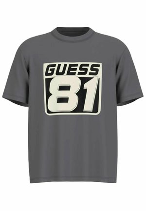 Maglietta grigia a maniche corte con la scritta "GUESS 81" in caratteri bianchi e neri in grassetto al centro sul davanti.
