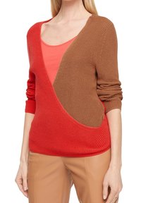 Pull en tricot rouge et marron avec un décolleté en V profond, tissu texturé, manches larges et un design en blocs de couleur contrastés. Superposé sur un top corail.