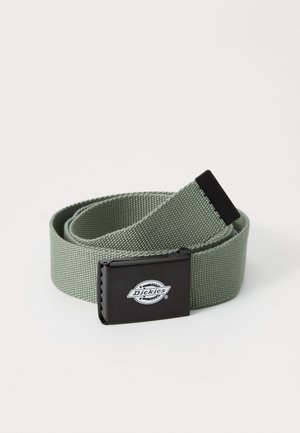 Ceinture en tissu tissé vert avec une boucle carrée en métal noir portant un logo. La ceinture a une surface texturée et est enroulée.