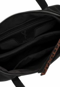 Juodas rankinės krepšys atidarytas, kad būtų matomas vidus su keliais užtrauktukais ir leopardų rašto užtrauktuko laikikliu.